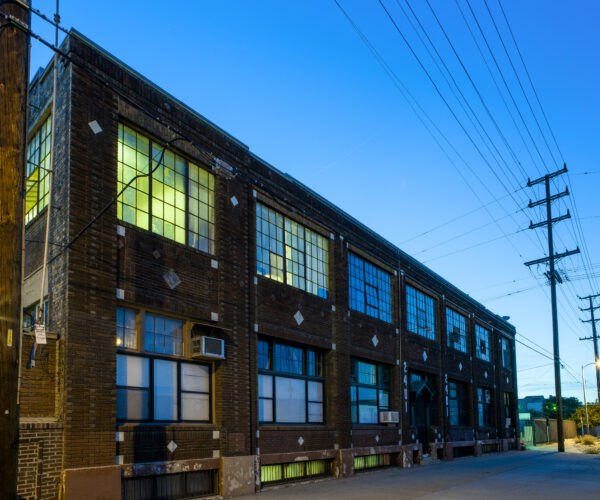 Two story brick building with light emanating from interior windows against dusky sky