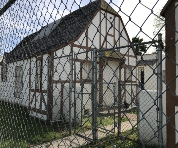 Derelict bungalow court behind chain link fence