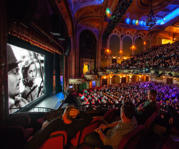 Crowd of people inside a movie palace watching a black and white movie.